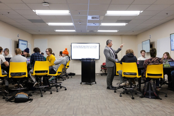 Instructor works with student groups in an active learning classroom with shared displays.