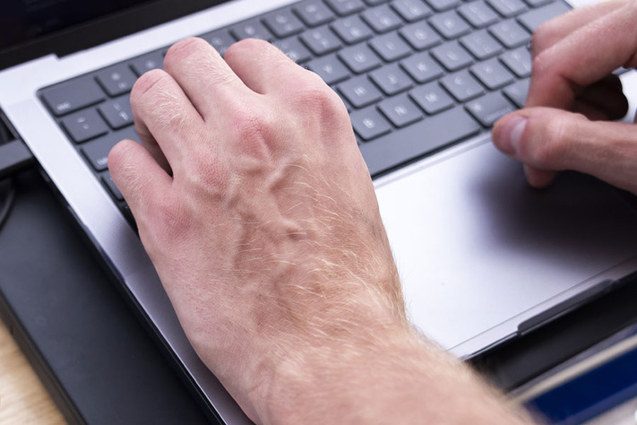Hands using a laptop keyboard and trackpad.