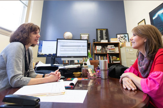 Staff members meet in an office, discussing information displayed on a computer monitor.