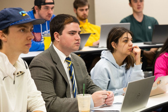 Students use laptops and take notes while participating in a classroom discussion.